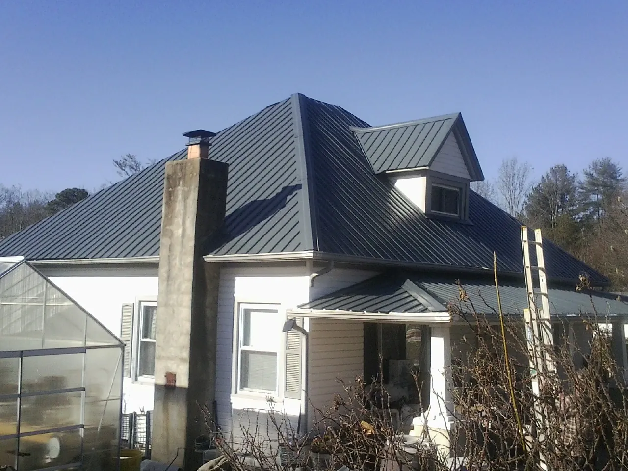 Dark blue standing seam metal roof on a white farmhouse with dormer — Slate & Tile Roof Repair by Roofing Brothers in Annapolis Junction