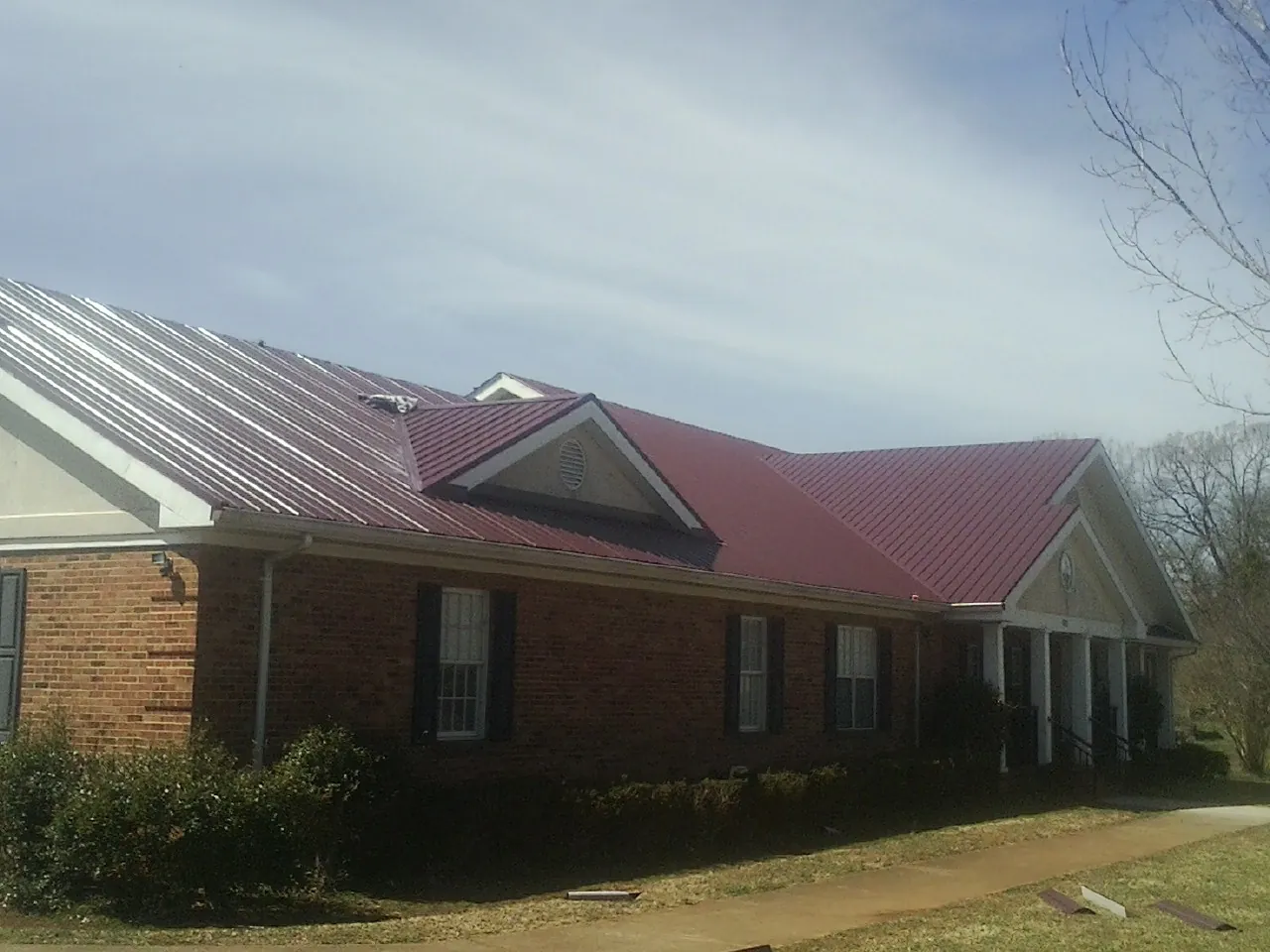 Red metal roof with gabled entries on a long brick building, from a Hail Damage Roof Repair job in Annapolis Junction