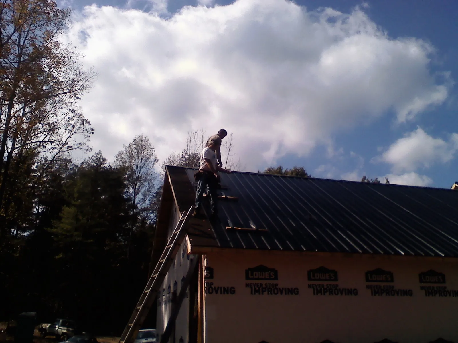 Roofer fastening dark metal panels high against a cloudy sky, from a Roof Inspection job in Annapolis Junction