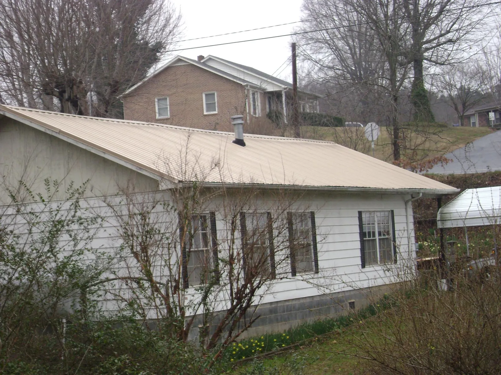 Tan metal roof on a white sided house set into a hillside — Commercial Roofing by Roofing Brothers in Annapolis Junction